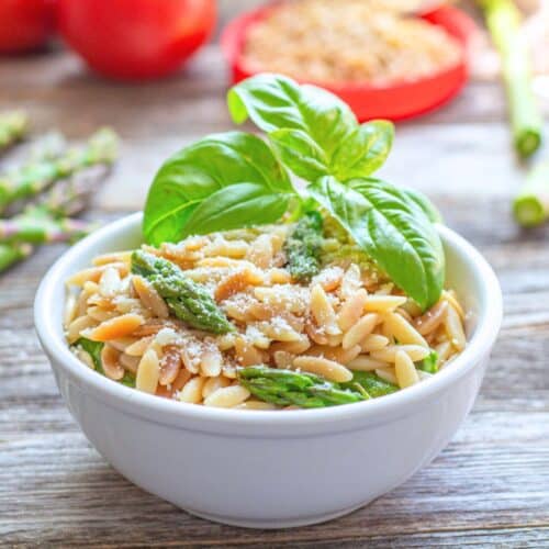 Toasted Orzo with asparagus topped with basil sprig in a bowl