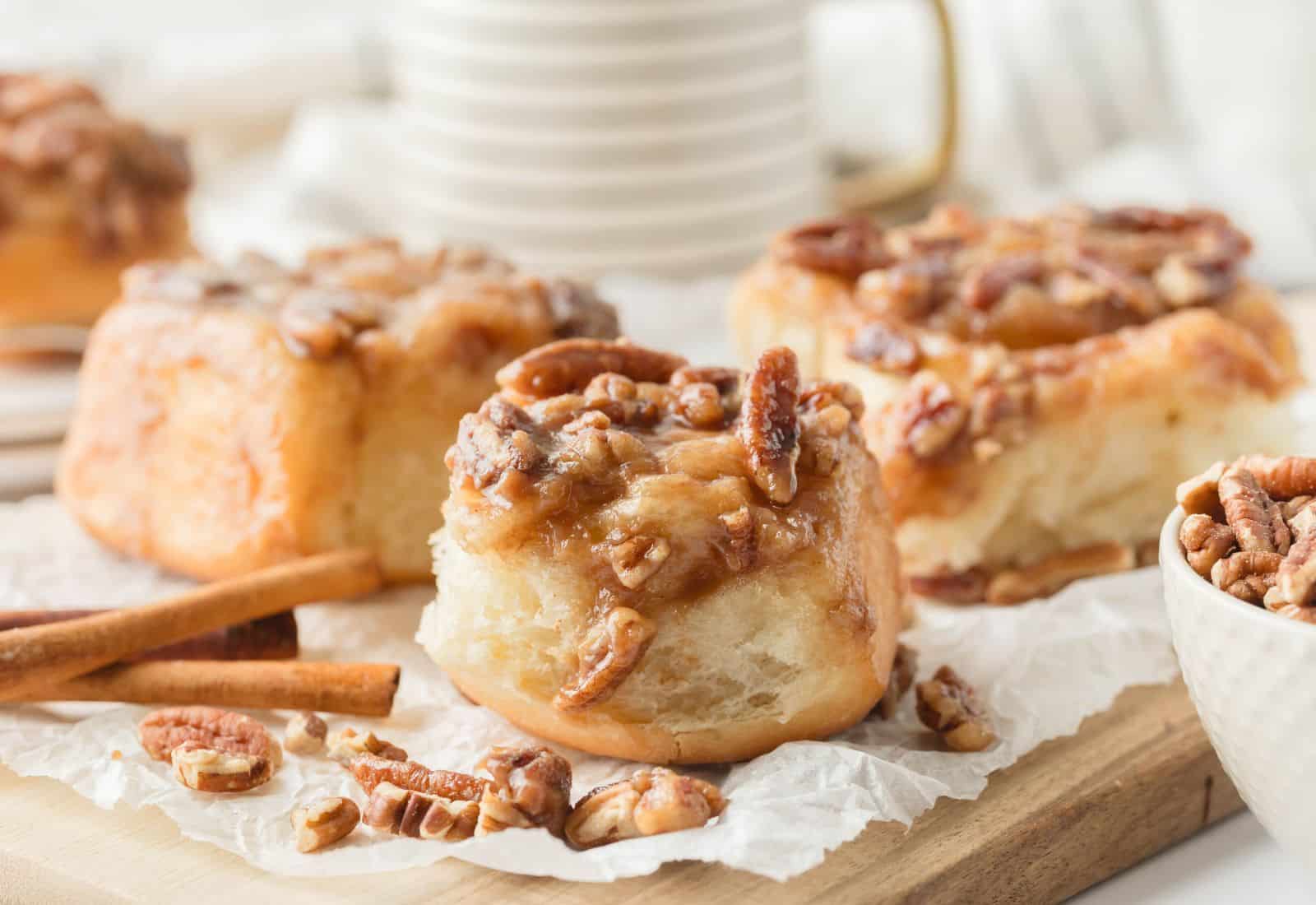 sticky buns surrounded by cinnamon sticks pecans and a coffee cup in the background