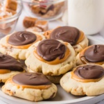 Shortbread cookies topped with caramel and chocolate stacked on a plate in front of a milk jug