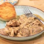 chicken and gravy on a blue plate with a biscuit and fork