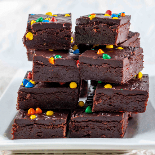 iced chocolate brownies topped with rainbow chips stacked on a plate