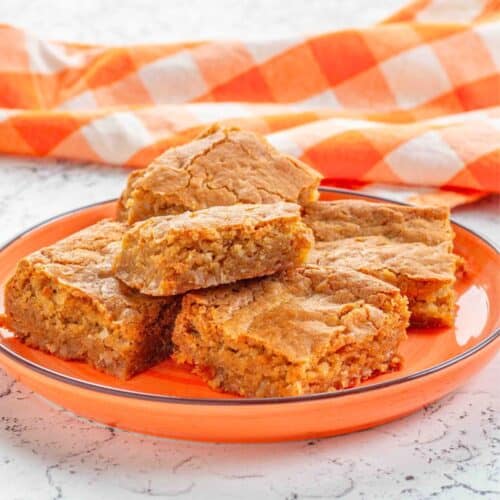 coconut blondies on an orange plate with an orange checked napkin in the background