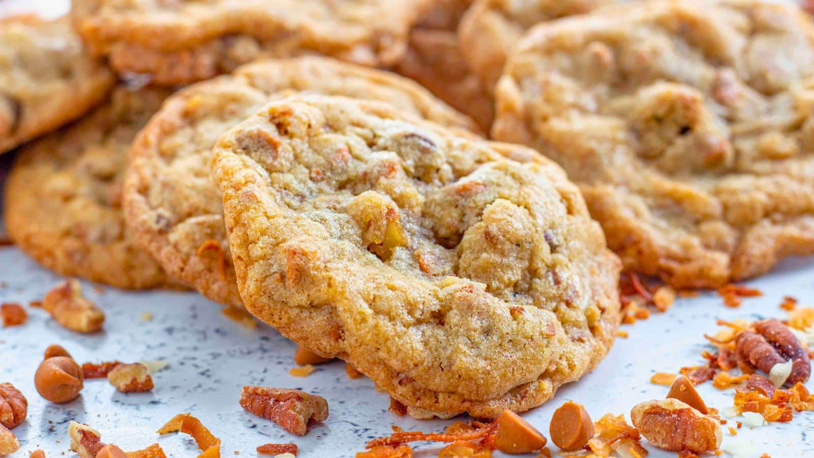 cinnamon chip cookies stacked on a board surrounded by cinnamon chips toasted coconut and nuts