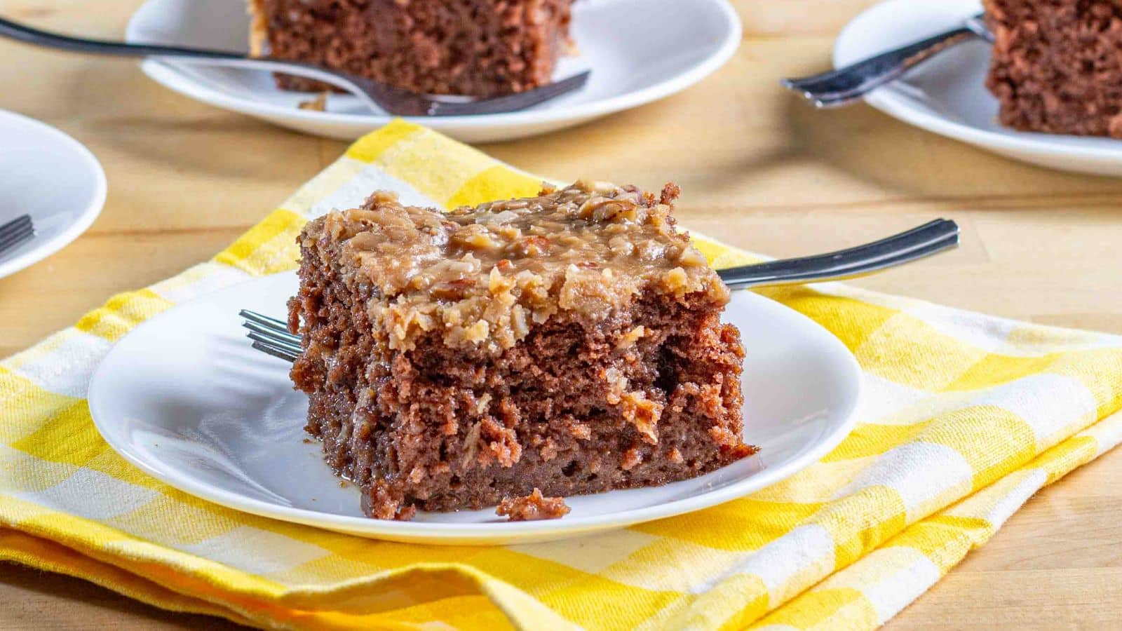 chocolate poke cake with german cake frosting on a plate with a fork sitting on a yellow checked napkin