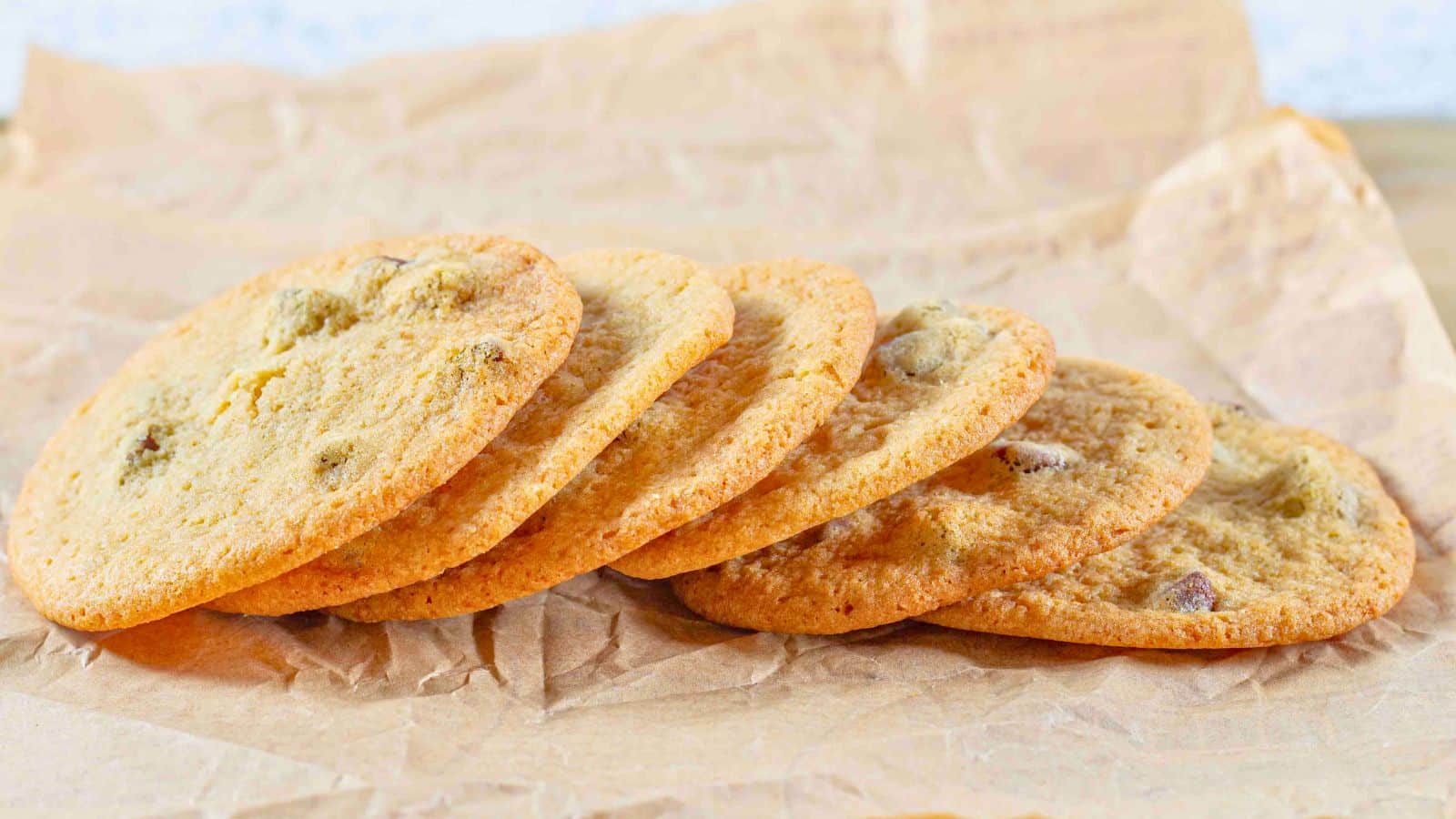 thin chocolate chip cookies stacked in a row on brown paper