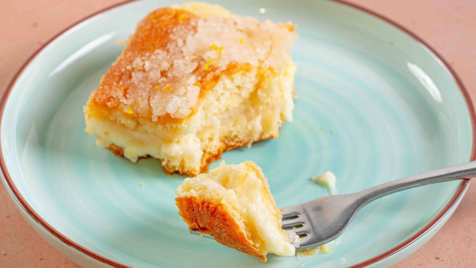 Lemon cream cheese bar on a plate with a bite on a fork on a teal plate