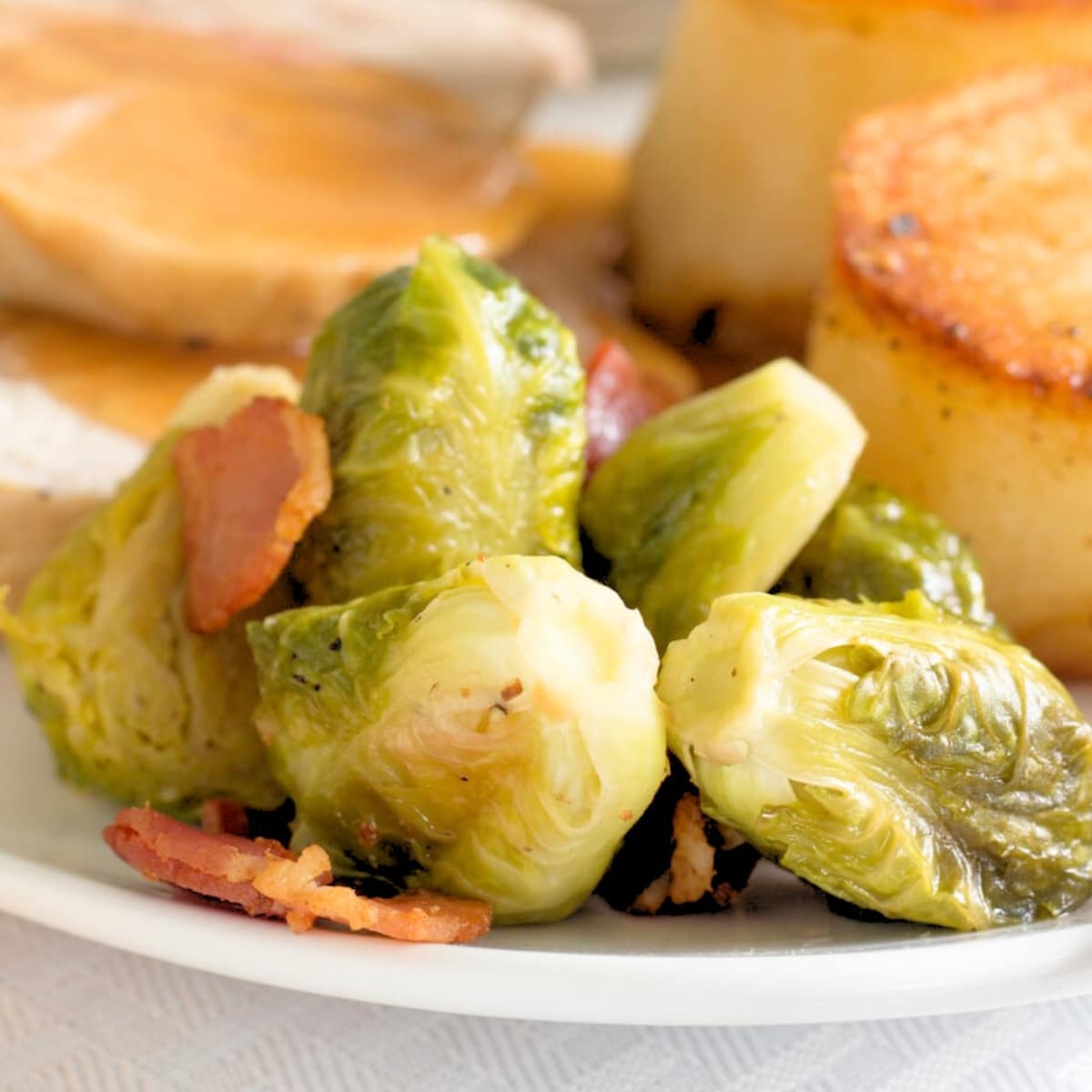 Brussels sprouts topped with bacon pieces in froont of potatoes