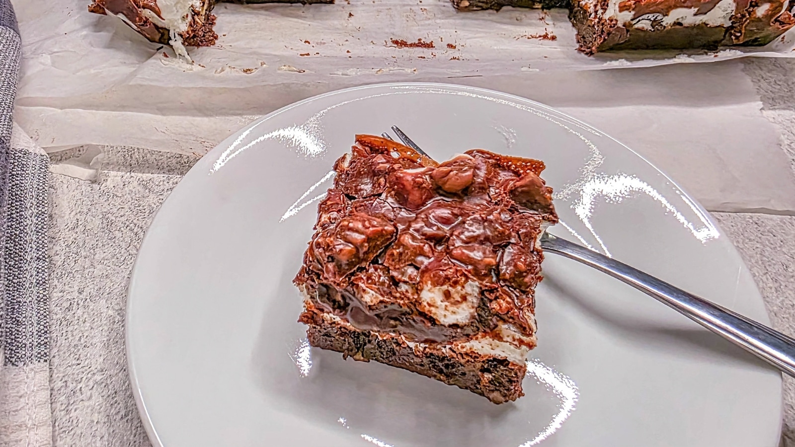 top view of fudge cake topped with marshmallows and chocolate glaze on a white plate with a fork