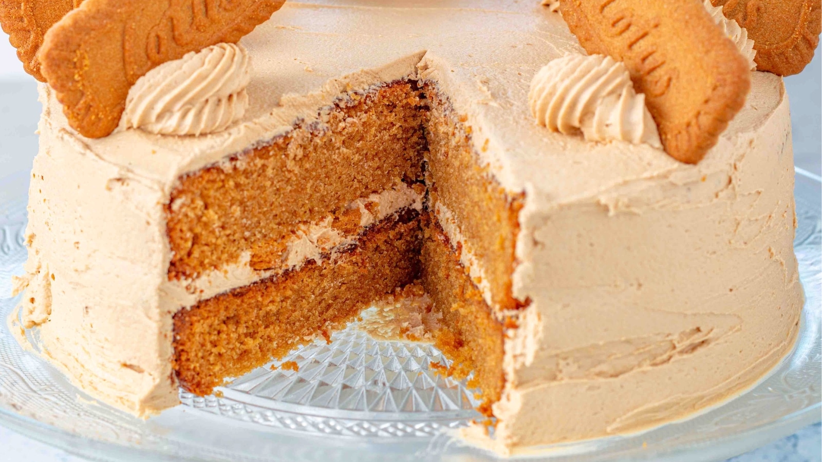 lotus biscoff cake with a slice missing on a glass cake plate