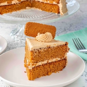 slice of layered biscoff cookie butter cake topped with a cookie butter frosting, frosting swirl and a whole biscoff cookie